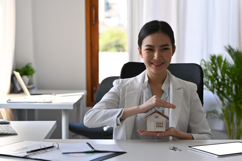 Beautiful asian woman hands protecting house model. Insurance or loan real estate concept.